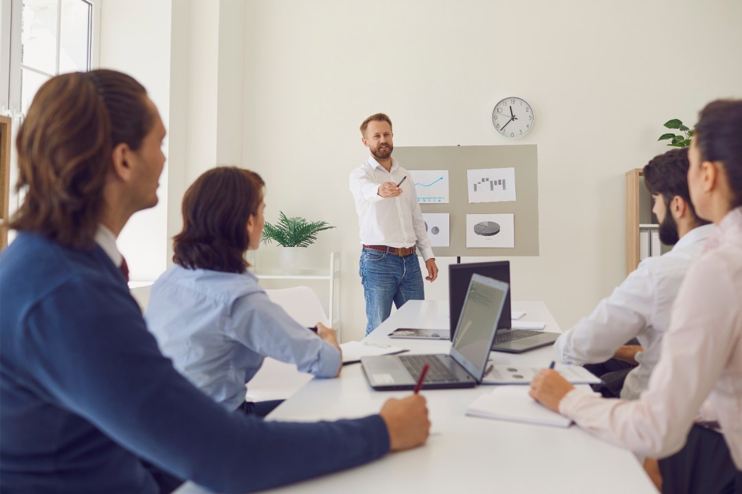 Instructor dicta una clase a un grupo de profesionales sentados frente a notebooks