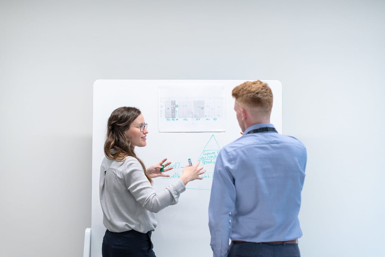 Dos profesionales conversan frente a una pizarra con diagramas en una oficina